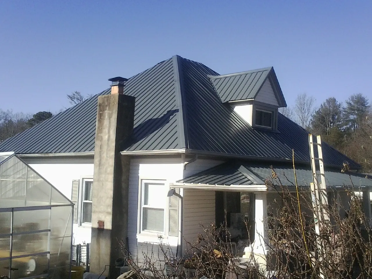 Dark blue standing seam metal roof on a white farmhouse with dormer — Slate & Tile Roof Repair by Roofing Brothers in Waukon