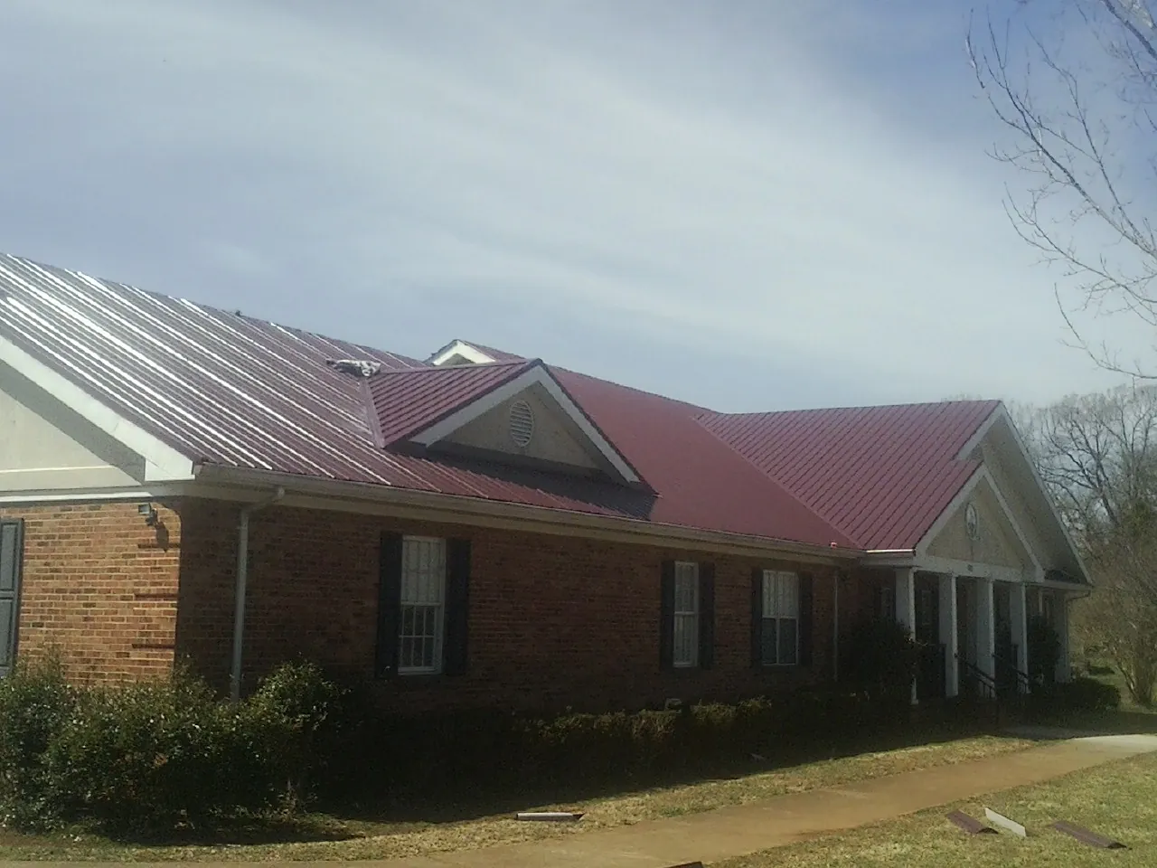Red metal roof with gabled entries on a long brick building, from a Hail Damage Roof Repair job in Waukon