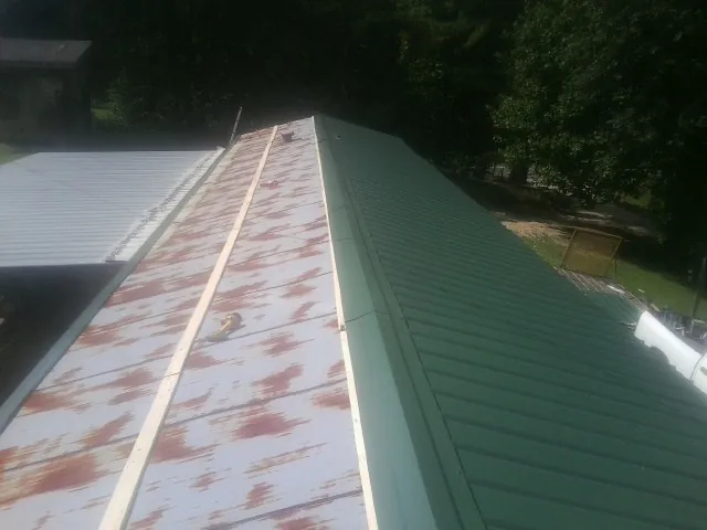 Old rusted panels beside newly installed green metal roofing — Wind Damage Roof Repair by Roofing Brothers in Waukon
