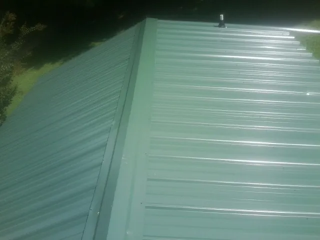 New green metal panels meeting at the ridge of a roof — Flat Roof Repair work by our crew in Waukon