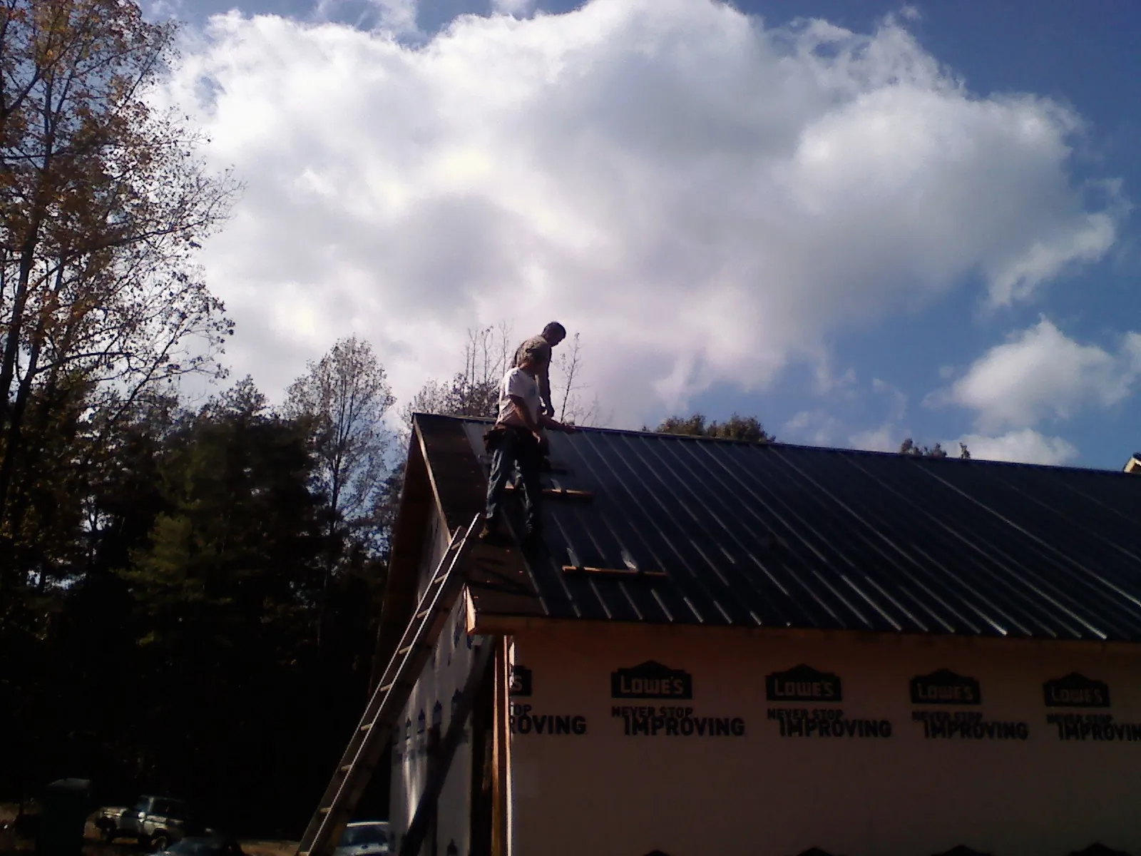 Roofer fastening dark metal panels high against a cloudy sky, from a Roof Inspection job in Waukon
