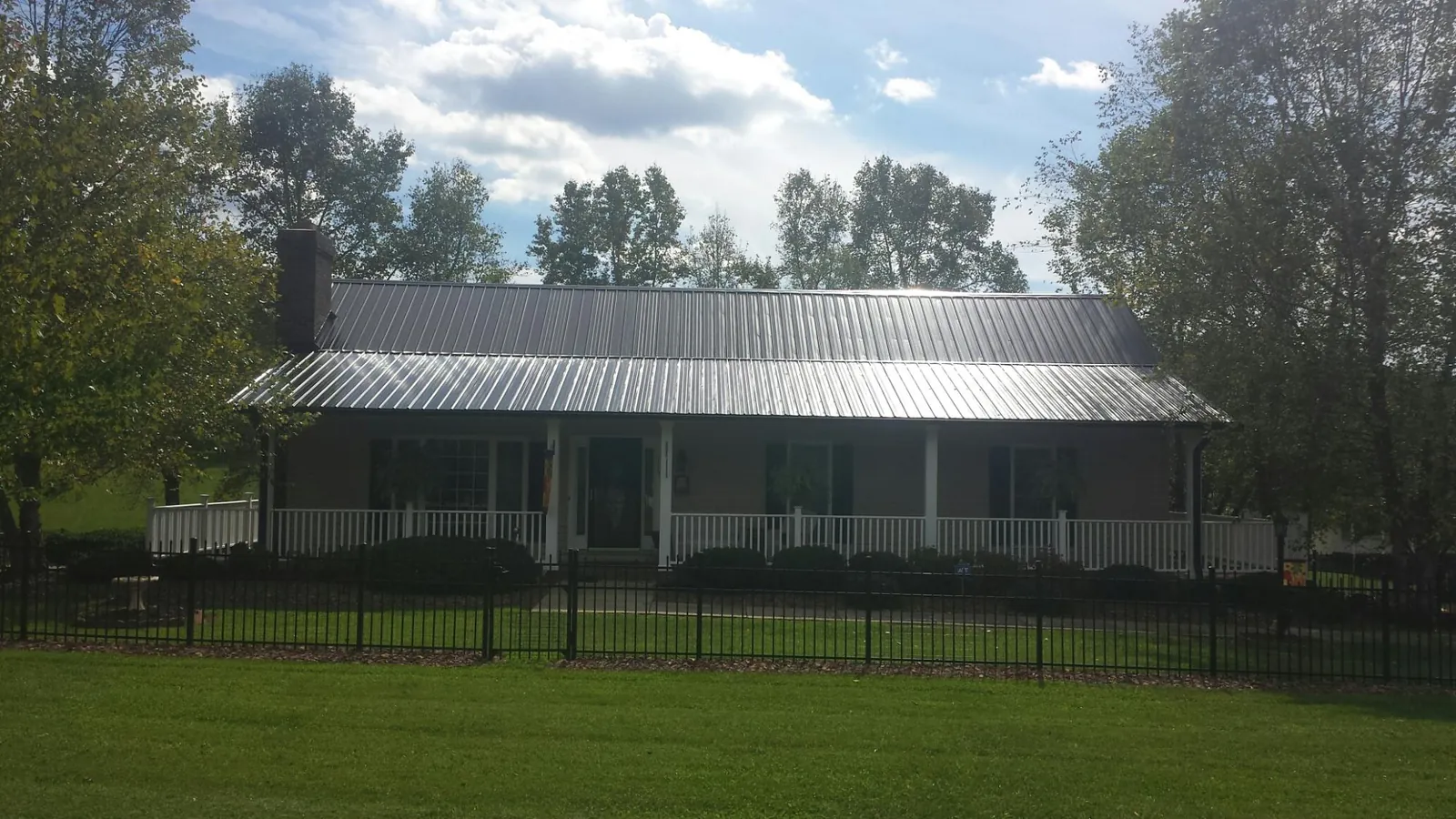 Gray metal roof on a brick ranch with a full width front porch — Gutter Guard Installation work by our crew in Waukon