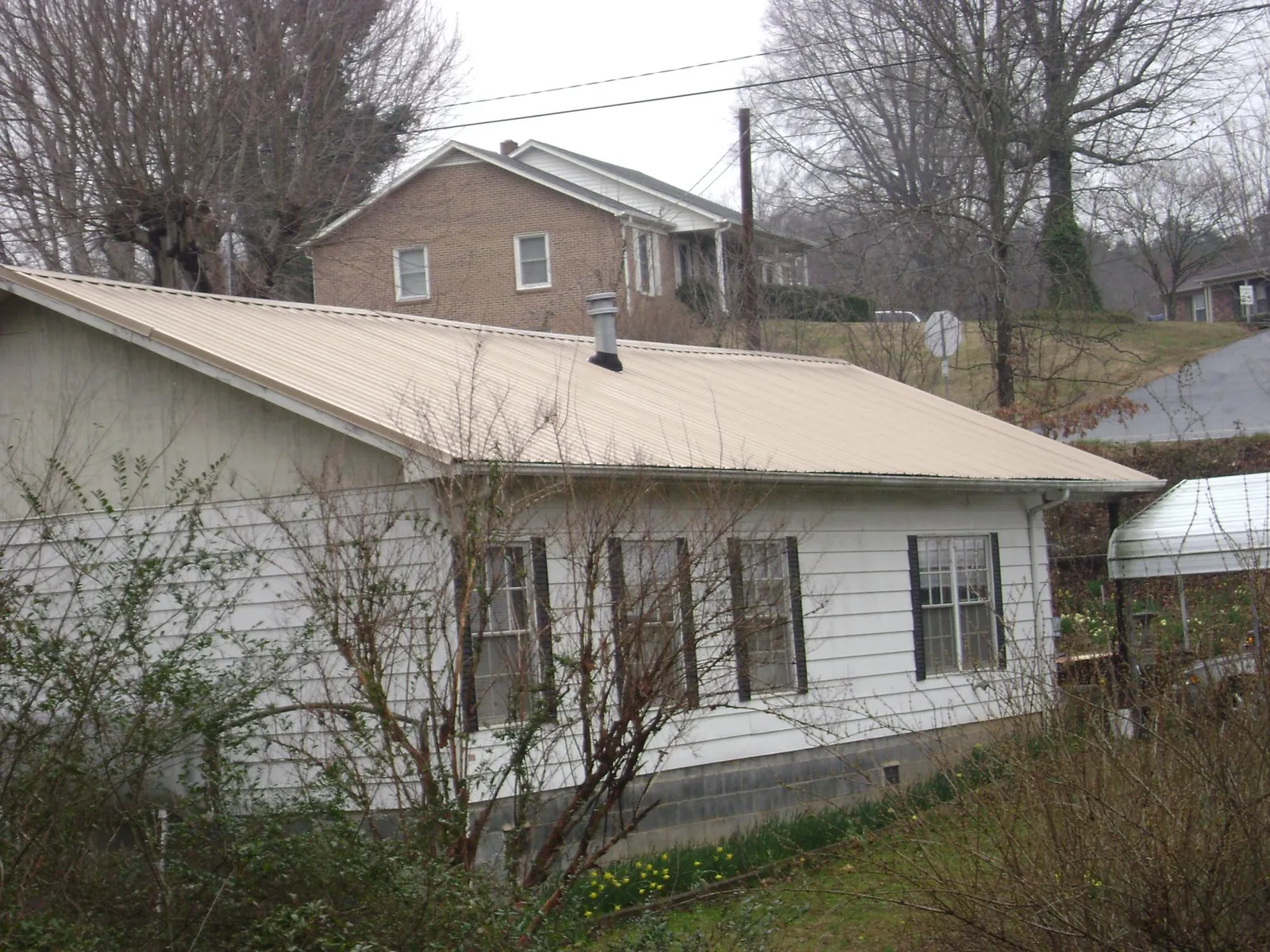 Tan metal roof on a white sided house set into a hillside — Commercial Roofing by Roofing Brothers in Waukon