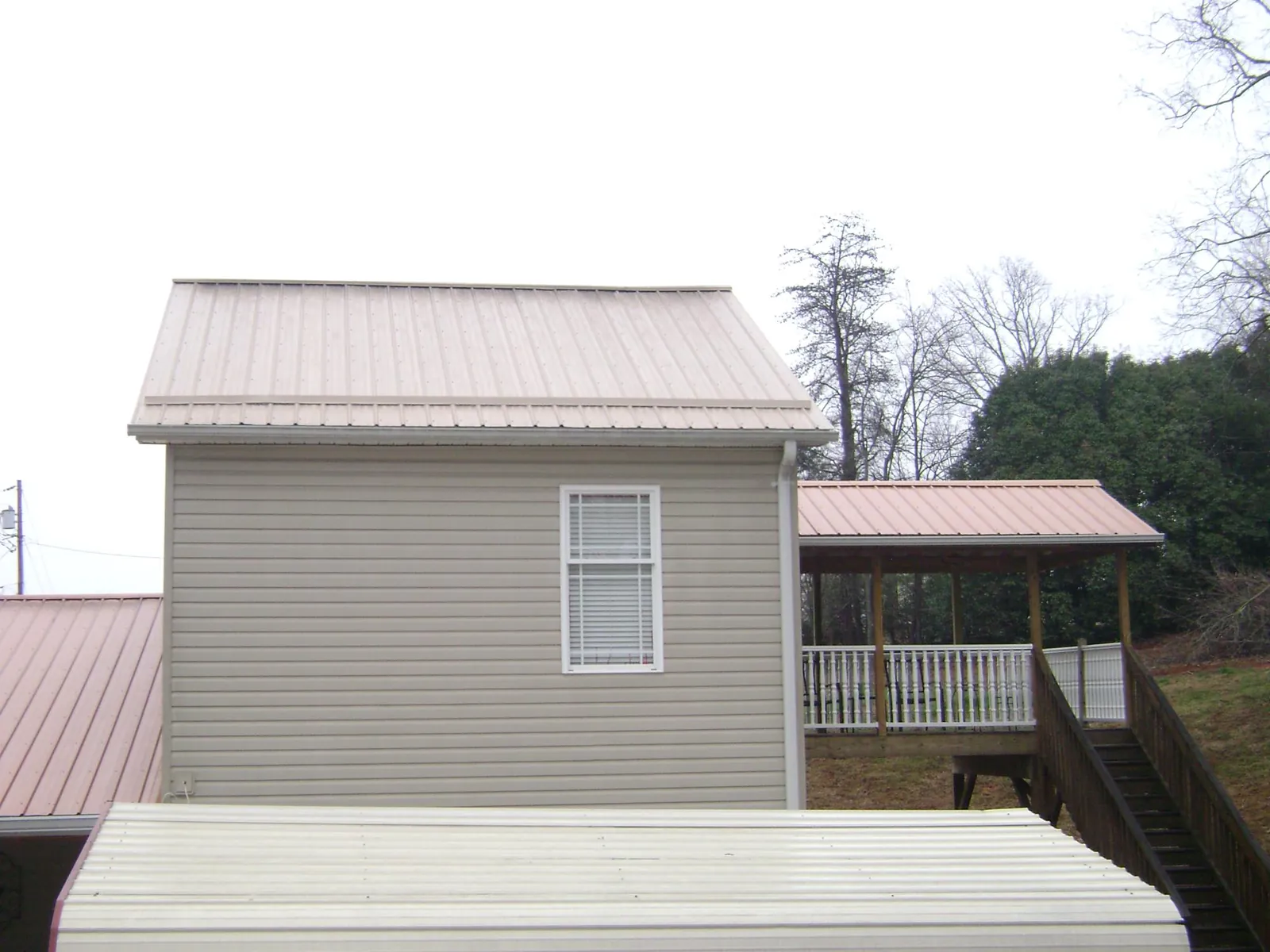 Tan metal roofs on a two story addition and attached porch, from a Roof Replacement job in Waukon